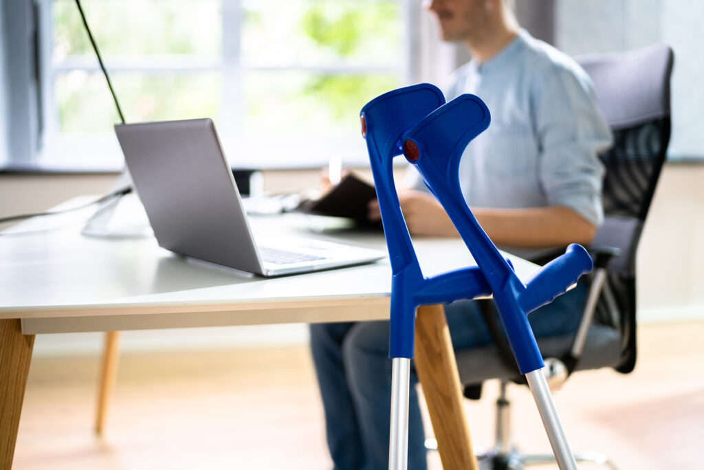 Injured employee using crutches at a desk in a workplace setting